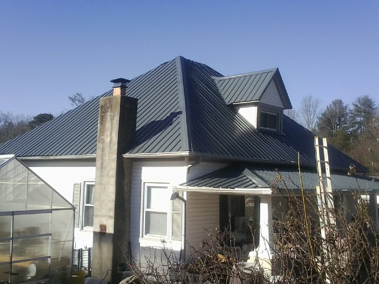 Dark blue standing seam metal roof on a white farmhouse with dormer — Slate & Tile Roof Repair by Roofing Brothers in Iron City