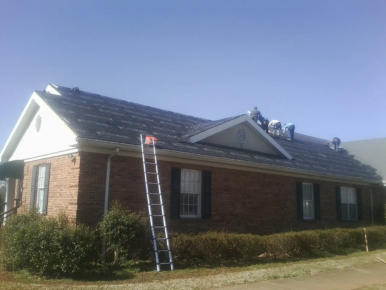 Crew tearing shingles off a brick ranch roof with a ladder set — Emergency Roof Repair work by our crew in Iron City