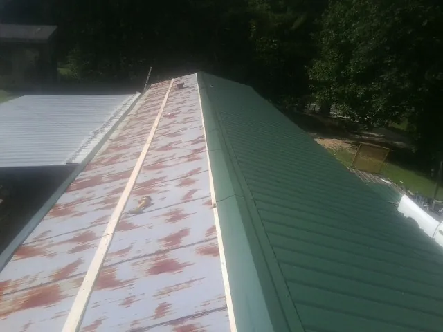 Old rusted panels beside newly installed green metal roofing — Wind Damage Roof Repair by Roofing Brothers in Iron City