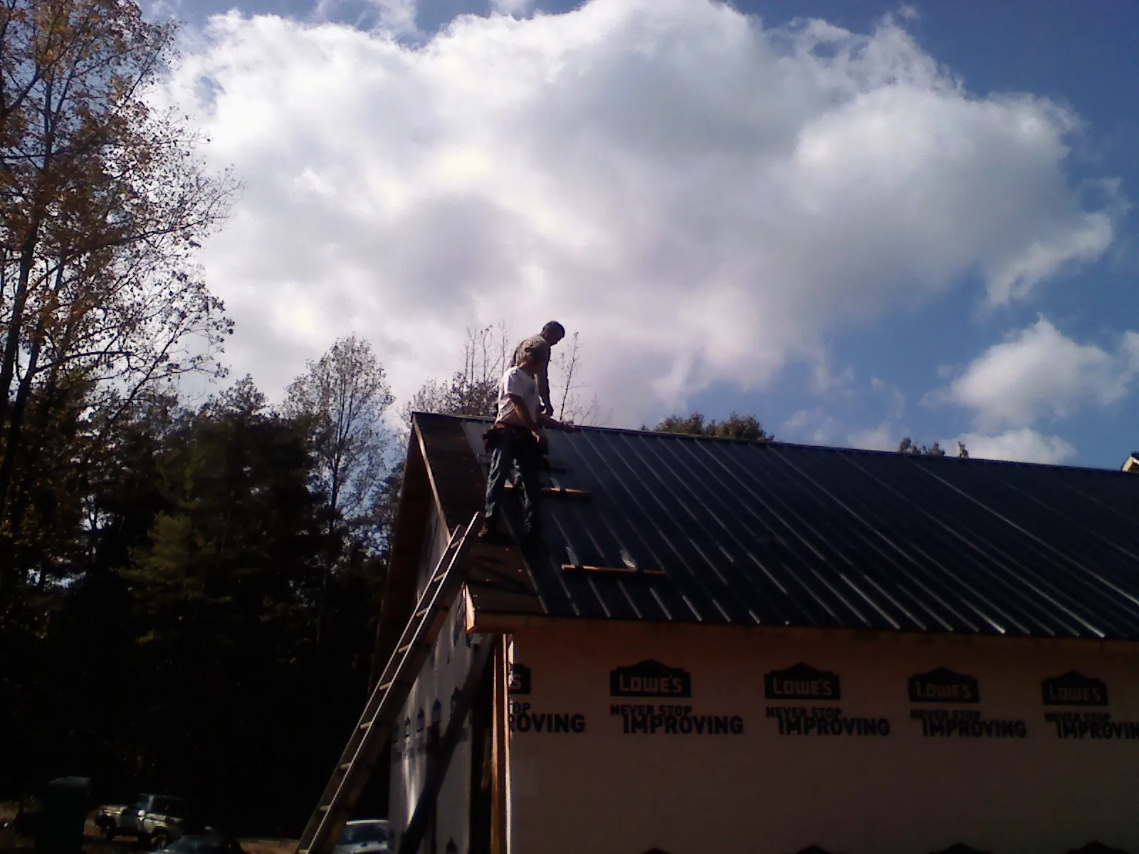 Roofer fastening dark metal panels high against a cloudy sky, from a Roof Inspection job in Iron City