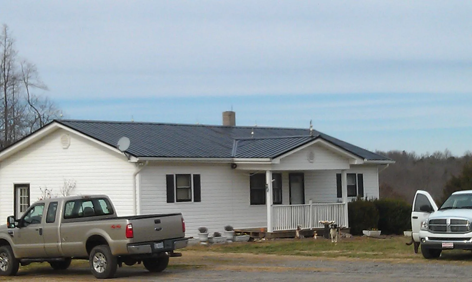 Finished dark metal roof on a white ranch home with work trucks parked in Iron City