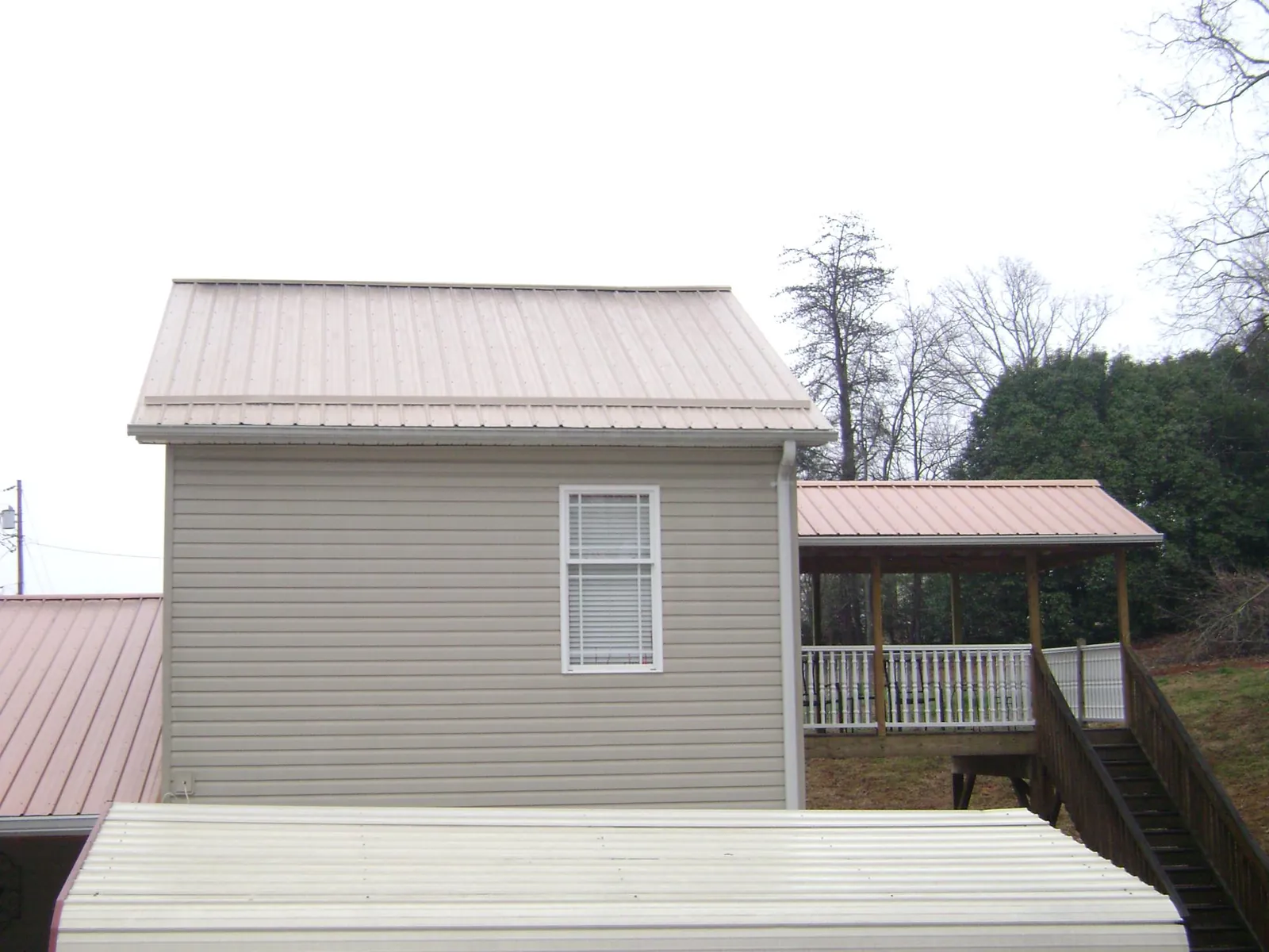 Tan metal roofs on a two story addition and attached porch, from a Roof Replacement job in Iron City